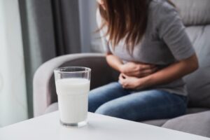 Woman having a bad stomach ache due to lactose intolerance with a glass of milk in the table