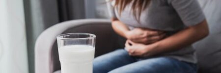 Woman having a bad stomach ache due to lactose intolerance with a glass of milk in the table